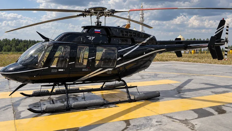 A black Bell 407 helicopter on a helipad