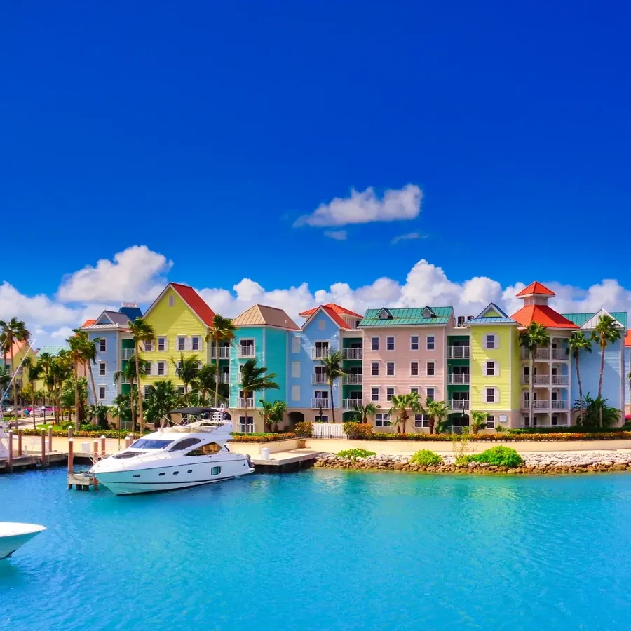 Pastel painted waterfront buildings with red and green roofs behind a marina, a white motor yacht at the dock and bright turquoise water in front