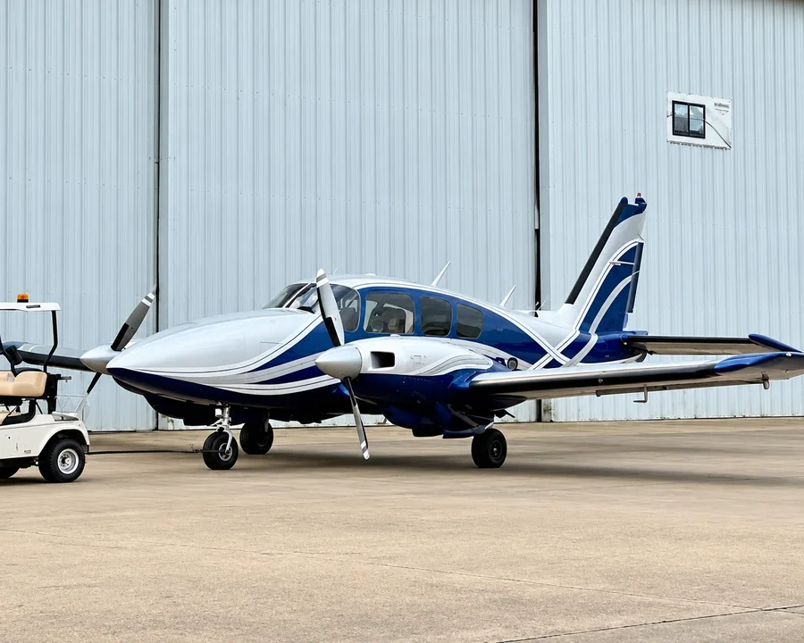 A blue and white Piper Aztec twin piston plane in front of a hangar